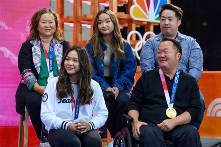 Who are Sunisa Lee siblings? Here’s everything to know about the Olympic gold medalist’s family and siblings details. Sunisa Lee is an American artistic gymnast. Nicknamed Suni, she performs at the Senior International Elite level. Morevoer, she is associated with the Midwestern Gymnastic center. Lee won gold in the women’s all-around competition at the Tokyo Olympics on 29 July. Besides her recent win, Sunisa has also tasted victory as a member of the team that won gold at the 2019 World Championships and silver at the Olympic Games. She is the first Hmong-American Olympic gymnast and has been part of the United States women’s national gymnast team since 2017. Graduating high school from South St. Paul Secondary School in Minnesota in June, Sunisa is committed to competing at Auburn University. Besides gymnastics, she is also interested in science and likes eating pasta. Sunisa Lee Siblings: Who Are Her Brothers And Sisters? Sunisa Lee has five siblings: two sisters named Shyenne and Evionn, and three brothers called Jonah, Lucky, and Noah. Among her siblings, Evionn, Jonah, Lucy, and Noah, belong to the younger group. Evionn has also competed in artistic gymnastics at the regional level. She is only 12 days apart from Shyenne by birth. Although none of her siblings have been in the spotlight as much as her, her siblings are probably happy for her recent success at the Olympics. Further, Evionn is the only one reported participating in sports. Sunisa Lee Parents And Family Background Regarding her parents, Sunisa Lee was born on March 9, 2003, to Yeev Thoj. Her mother was a healthcare worker. But, her biological father’s identity hasn’t been disclosed to the public but, her stepfather is John Lee. Apparently, her mother met John when she was 2 years old. Although John is said to be her father, he never legally married Yeev. Further, Yeev lists her relationship status as married on Facebook. Lee, however, decided to change her last name to her father’s. Both of her parents immigrated from Laos and were part of the large Hmong families. It seems their families escaped Laos, making the dangerous trek across the Mekong River to refugee camps in Thailand. They later found themselves in the United States. Her father was partially paralyzed due to an accident in August 2019. Her father has 10 siblings, all living in the Minneapolis-St. Paul area. Her huge family, however, fell victim to the pandemic. Apparently, her aunt and uncle died in the summer due to COVID.